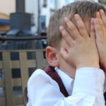 Un bambino imbarazzato si nascondo il viso con le mani