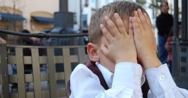 Un bambino imbarazzato si nascondo il viso con le mani