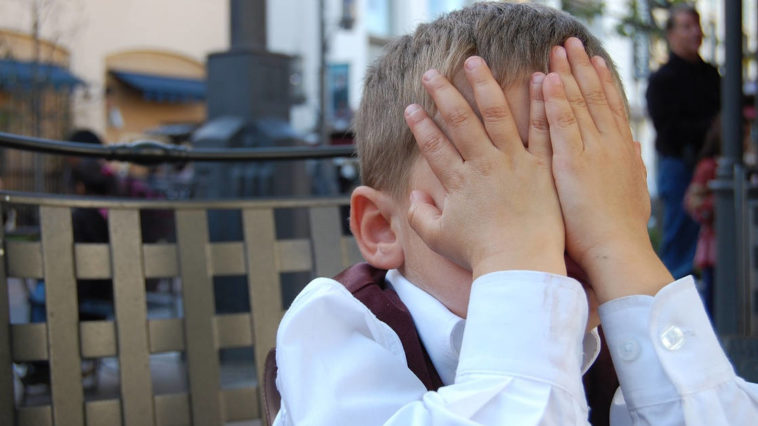 Un bambino imbarazzato si nascondo il viso con le mani