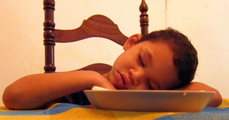 Bambino si addormenta al tavolo dopo aver mangiato un pasto abbondante che gli ha causato sonno