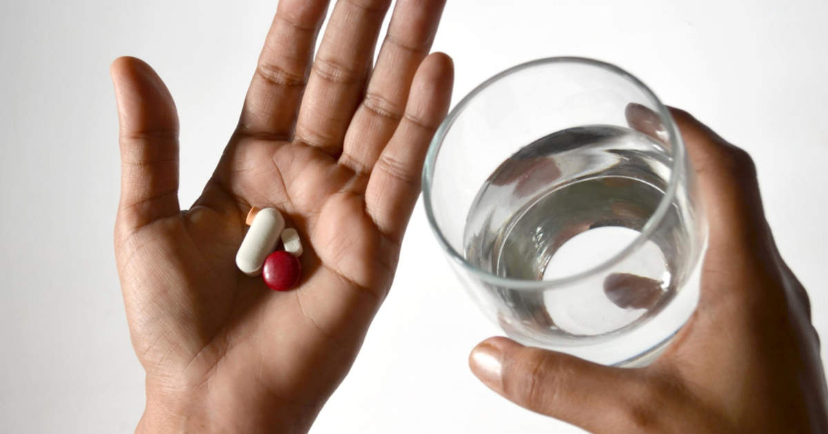 Un uomo ingoia una medicina in pillola con un bicchiere d'acqua ma ha paura di soffocare