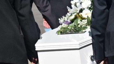 Funerale con persone che trasportano una bara bianca con dei fiori per dire condoglianze