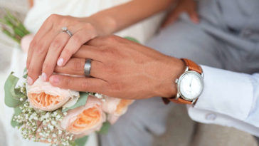sposi che si tengono per mano tenendo bouquet e orologio