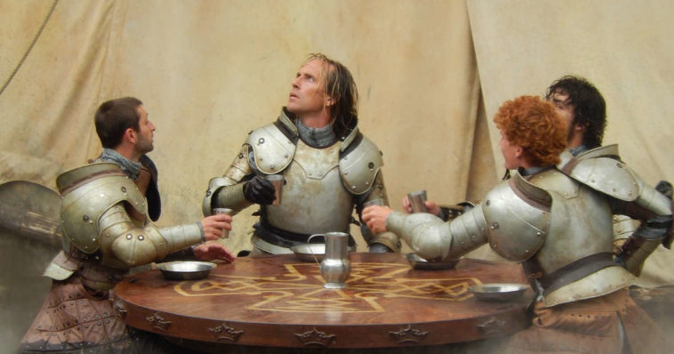 Cavalieri con armatura seduti attorno un tavolo rotondo mentre bevono del vino e mangiano