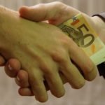 Due mani che si stringono, scambiandosi delle banconote