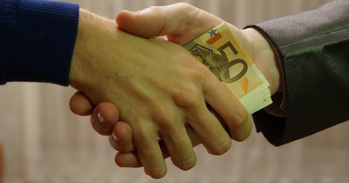 Due mani che si stringono, scambiandosi delle banconote
